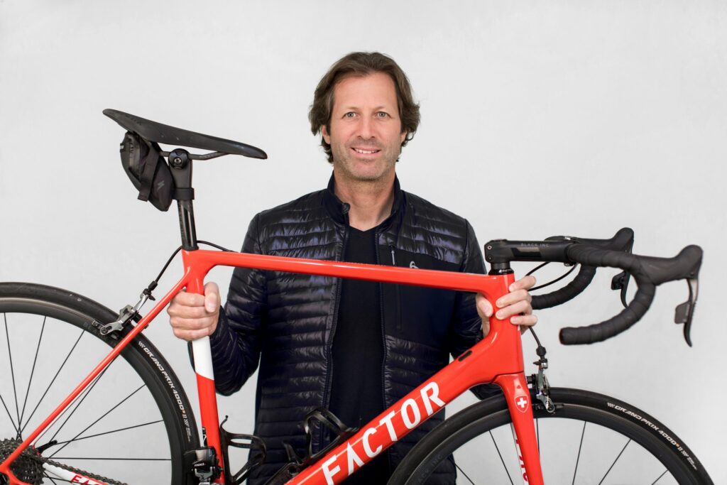 Man holding a red racing bike in front of a neutral background and smiling at the camera.